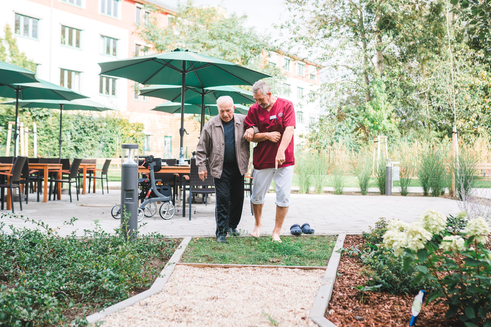 Seniorendomizil Bernau: Pflegefachkraft läuft mit Bewohner über Sinnespfad